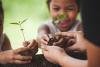 Happy family mother and daughter having fun to holding young tree in hands for planting in black soil together